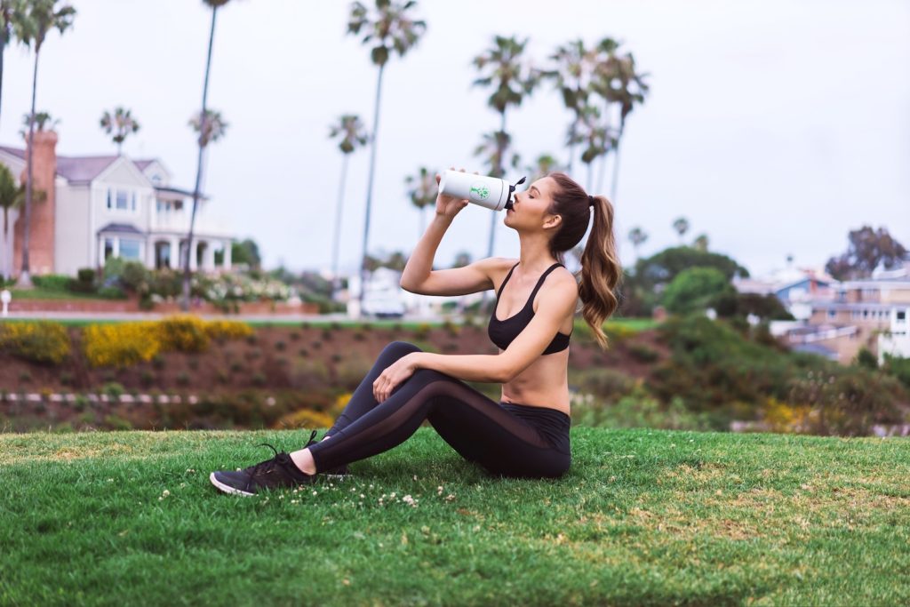 woman in black sports bra and black leggings sitting on green grass field during daytime