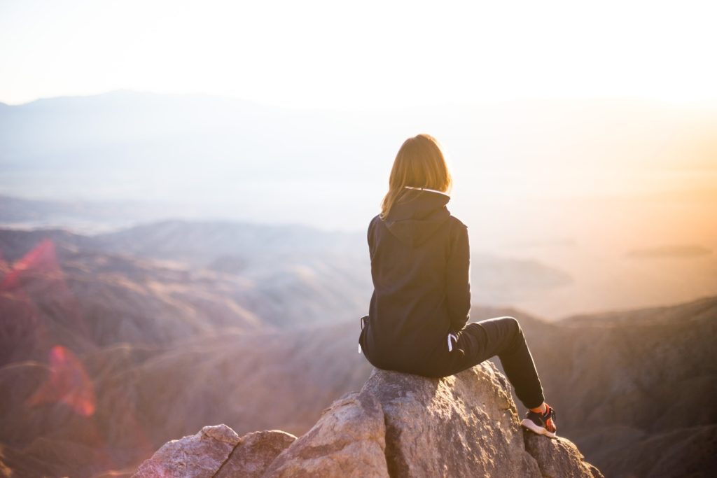 person, der sidder på toppen af ​​grå sten med udsigt over bjerget i dagtimerne